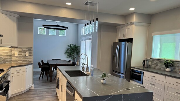 A modern kitchen with a large island, stainless steel appliances, and a dining area with a view. - Modern Remodeled Irvine Northwood Home (Irvine)
