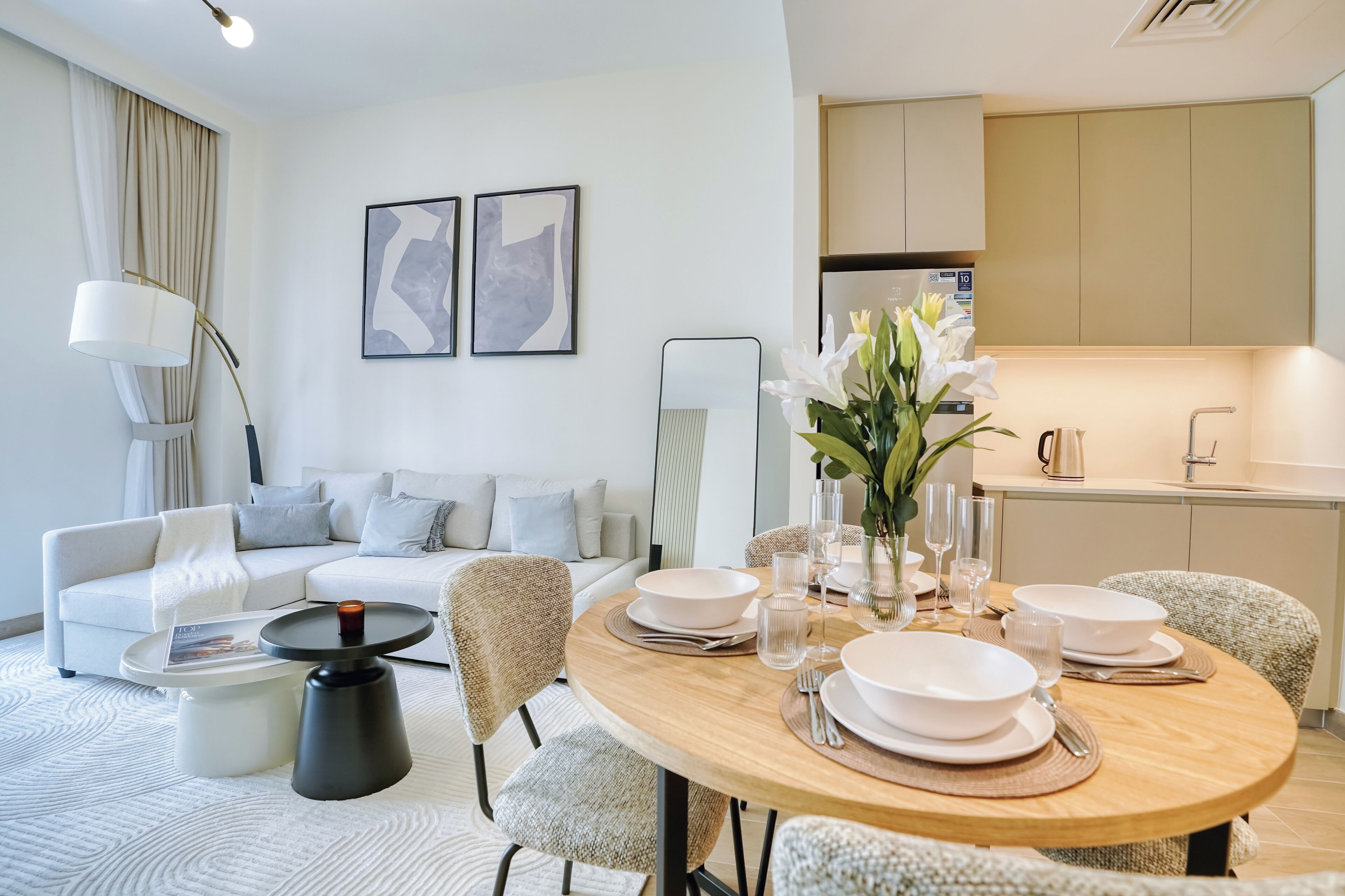 A modern living room with a dining area, a sofa, a coffee table, and a kitchen in the background.