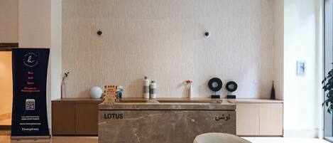 Una recepción con mostrador de mármol que lleva la etiqueta "LOTUS", un mueble de madera, un jarrón con flores y una pequeña mesa redonda.