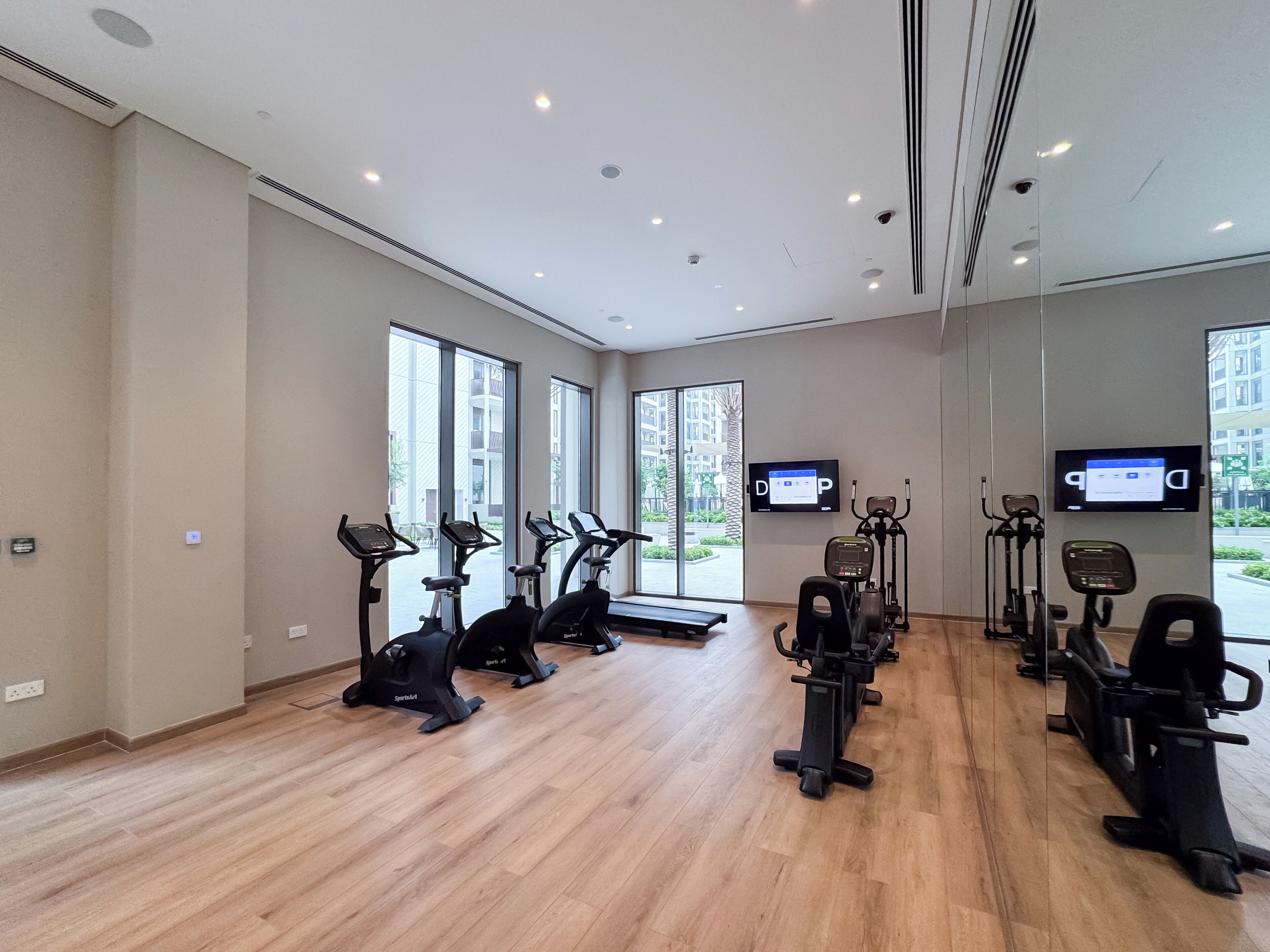 A gym with cardio machines, a TV screen, and large windows.