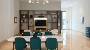 Een moderne eetruimte met een grote tafel, groene stoelen, een kroonluchter en een televisie aan de muur.