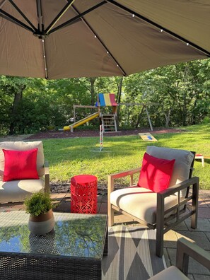 Ein Außenbereich mit Terrasse, Tisch, Stühlen und einer Spielanlage im Hintergrund.