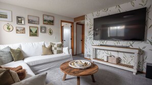 Ein Wohnzimmer mit einem weißen Sofa, einem runden Holztisch und einem Flachbildfernseher, der an einer Wand mit Blütentapete befestigt ist.