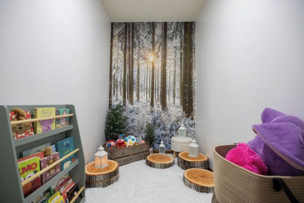 A cozy reading nook with a bookshelf, a small Christmas tree, and a basket with plush toys.