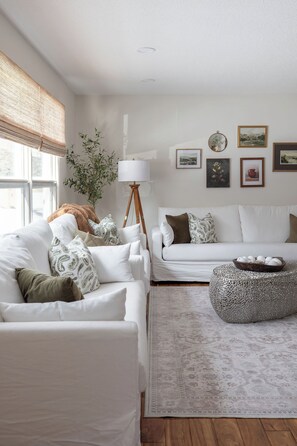 A living room with a white sofa, a round ottoman, and a patterned rug.
