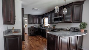 A modern kitchen with dark wood cabinets, a large island, stainless steel appliances, and pendant lighting.