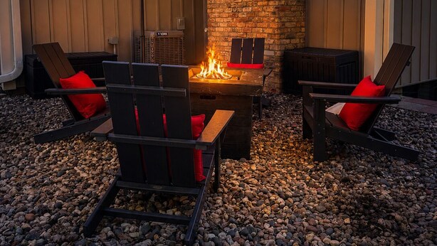 An outdoor patio with a fire pit, two lounge chairs, and a red umbrella.