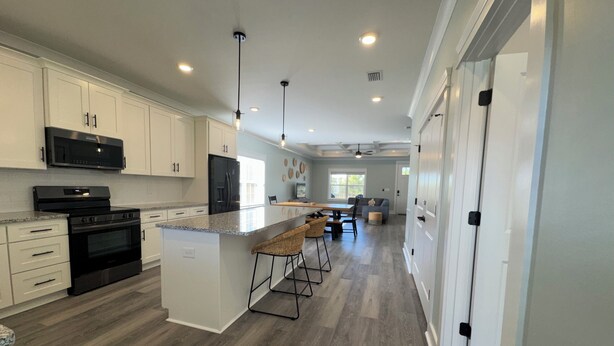 A modern kitchen with white cabinets, a black stove, and a large island with bar stools.