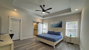 A bedroom with a bed, a ceiling fan, a window with blinds, and a door leading to a bathroom.