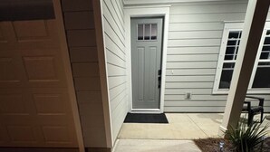 A covered entryway with a grey door, a concrete path, and a small garden area with plants.
