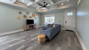 A spacious living room with a sectional sofa, a television on a wooden cabinet, and decorative wall art.