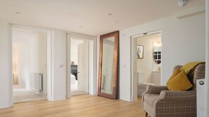 A spacious room with wooden flooring, a plaid armchair with a yellow pillow, and a large mirror.