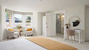 A bedroom with a large bed, two armchairs, a desk, and a mirror.