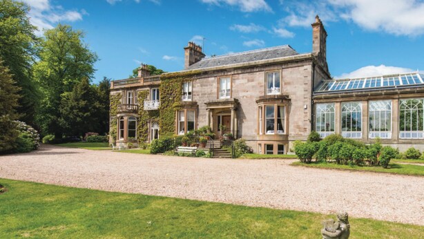 A large, historic stone building with multiple windows and a conservatory.