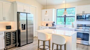 A modern kitchen with white cabinetry, stainless steel appliances, and a large island with bar stools.