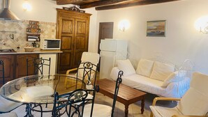 A cozy living room with a glass-top dining table, a sofa, and a kitchenette area.