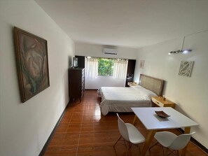 Ein Schlafzimmer mit einem Bett, einem Schreibtisch, Stühlen, einer Kommode und einem Bild an der Wand.