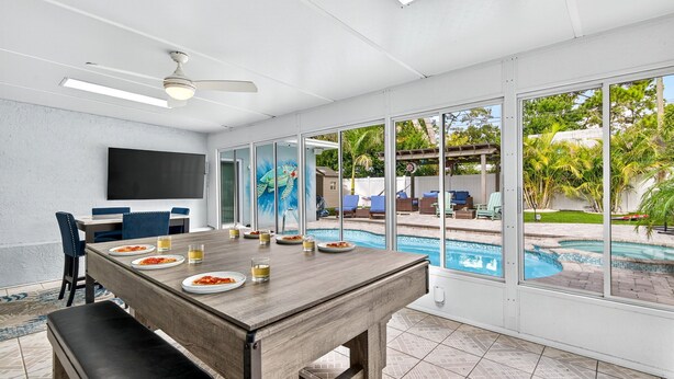 A dining area with a pool view, a ceiling fan, and a flat-screen TV. - Tropical Oasis Heated Pool • Spa • Pool Table • Grill • Games • Beach 15 Minutes (Seminole)