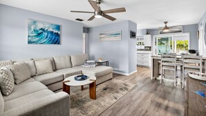 A modern living room with a sectional sofa, a coffee table, and a dining area with a kitchen in the background. - Tropical Oasis Heated Pool • Spa • Pool Table • Grill • Games • Beach 15 Minutes (Seminole)