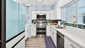 A modern kitchen with white cabinetry, stainless steel appliances, a patterned backsplash, and a large window with a decorative bird. - Tropical Oasis Heated Pool • Spa • Pool Table • Grill • Games • Beach 15 Minutes (Seminole)