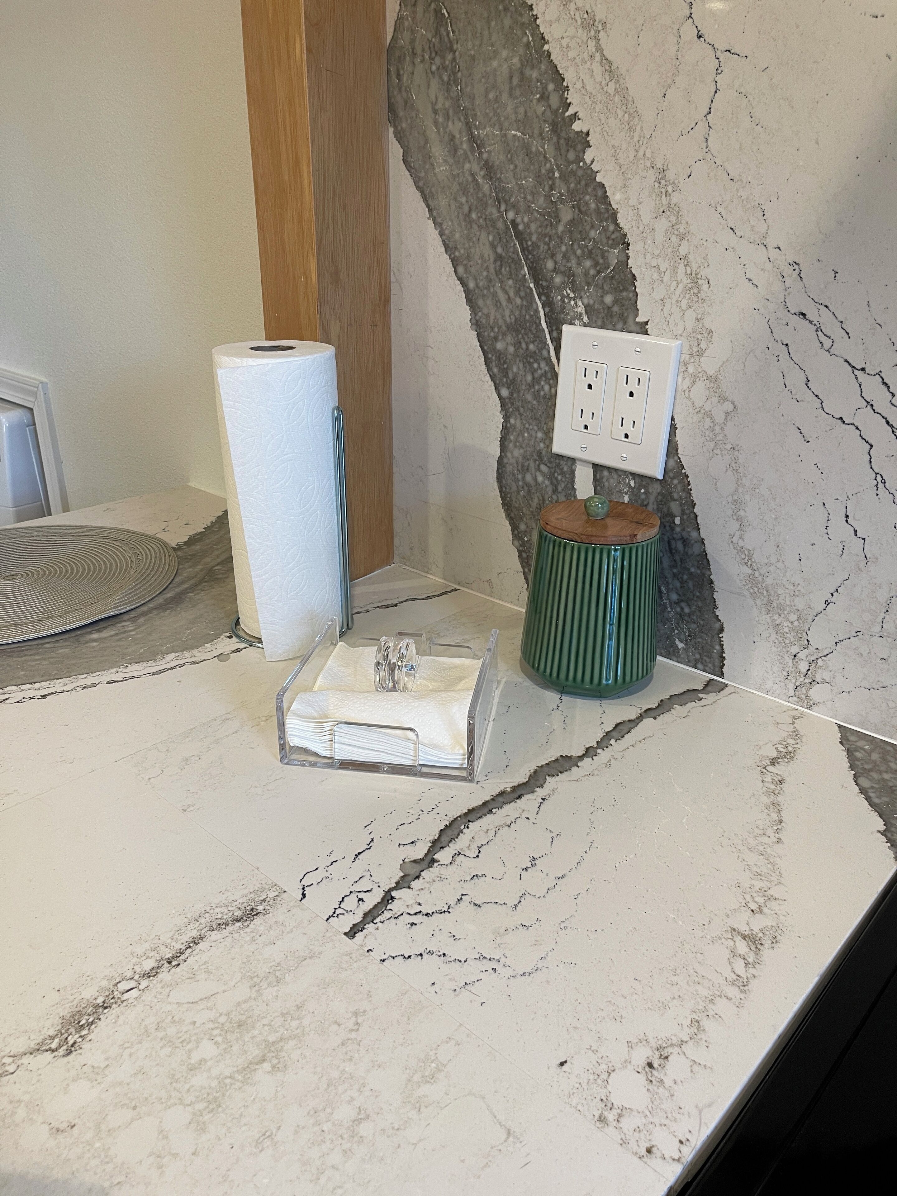 Una encimera de mármol con un dispensador de toallas de papel, un organizador de vidrio y un candelabro verde.