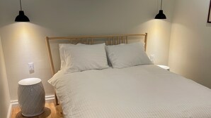 Een slaapkamer met een houten bed, twee bedlampen, een klein raam en een nachtkastje met een lamp.