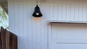 Een witte garage met een zwarte buitenlamp en een witte laadpaal voor elektrische voertuigen bevestigd aan de muur.