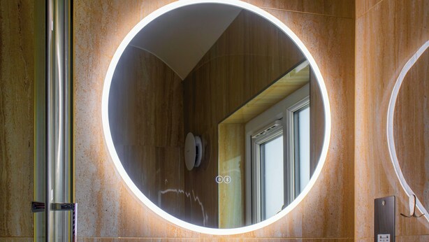 A bathroom with a circular mirror, wooden walls, and a visible door leading to another room.