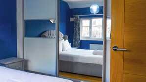 A bedroom with a bed, a bedside table, a wardrobe, and a window with curtains.