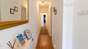 A hallway with wooden flooring, white walls, and a mirror on the left. There are framed pictures on the wall and a fire action plan on a shelf.