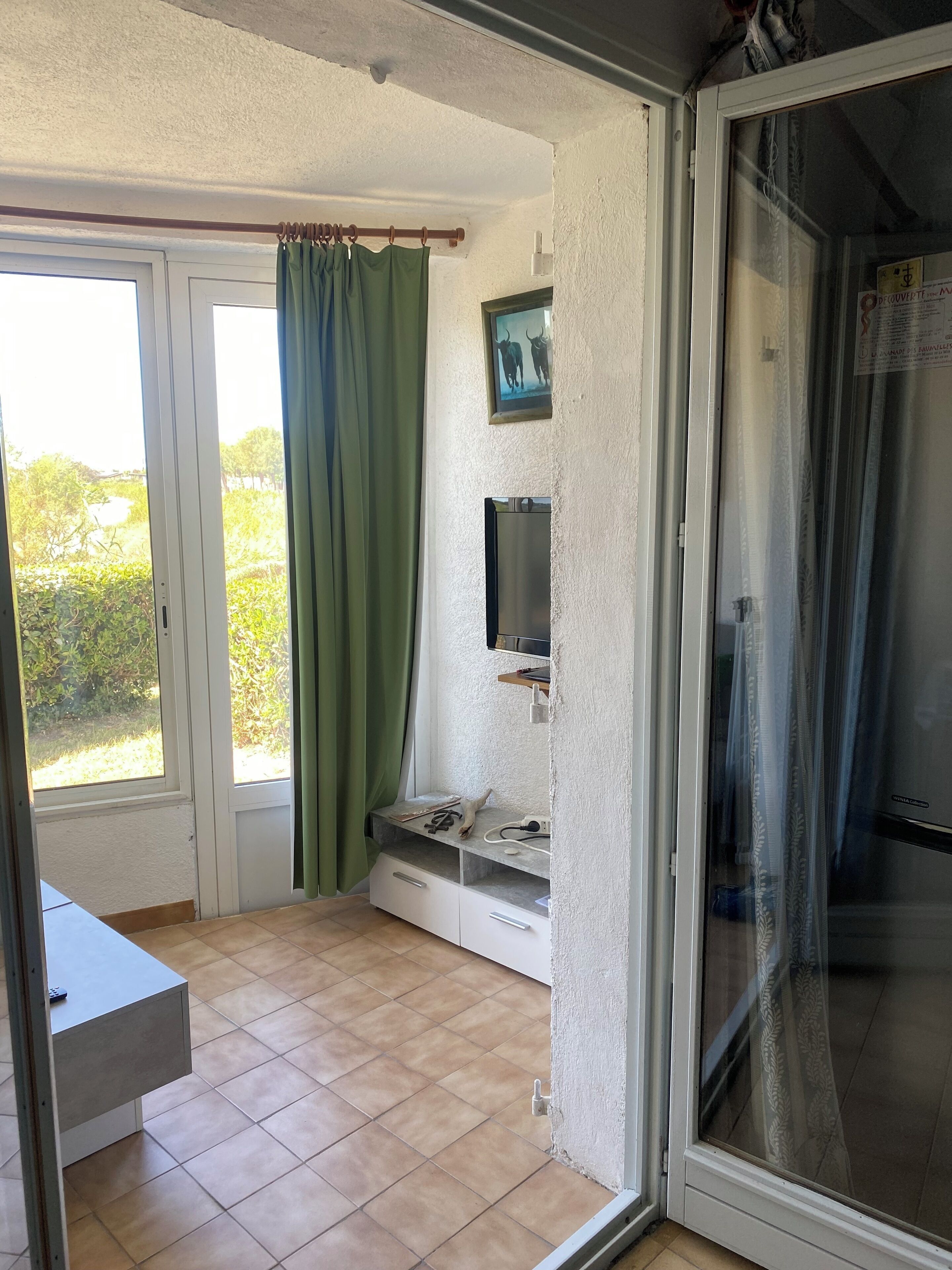 Een kamer met een schuifdeur, een klein tafeltje, een televisie op een plank en uitzicht op groen.