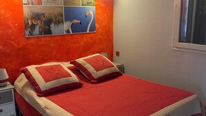 A bedroom with a red and white bedspread, a nightstand with a lamp, and a wall with framed pictures. - Apartment les saintes maries de la mer (Saintes-Maries-de-la-Mer)