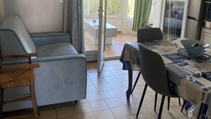A living room with a sofa, a dining table with chairs, a small table with a bowl, and a sliding glass door leading to an outdoor area. - Apartment les saintes maries de la mer (Saintes-Maries-de-la-Mer)