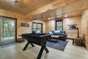 A cozy wooden cabin interior with a foosball table, a sofa, and a framed wildlife picture on the wall.