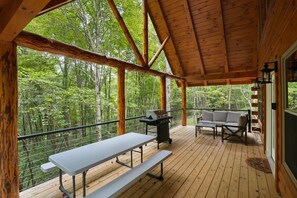 A covered deck with a picnic table, grill, and outdoor seating. - The Lazy Bear | Hocking Hills, Covered Hot Tub (Logan)