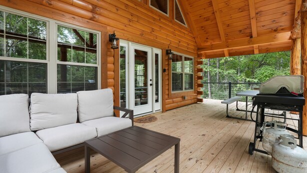 A wooden deck with a sofa, table, grill, and propane tanks.