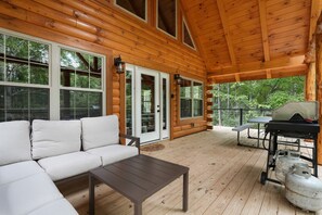 A wooden deck with a sofa, table, grill, and propane tanks.