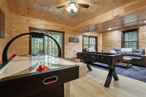 A wooden cabin interior with a foosball table, a pool table, and a sofa in a cozy living area. - The Lazy Bear | Hocking Hills, Covered Hot Tub (Logan)
