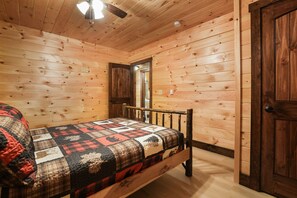 Un dormitorio de cabaña de madera con una cama, un ventilador de techo y una puerta.