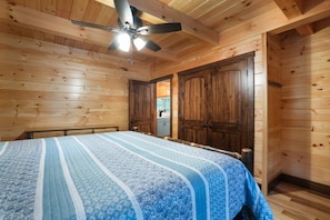 A wooden-paneled bedroom with a bed, a ceiling fan, and wooden doors.