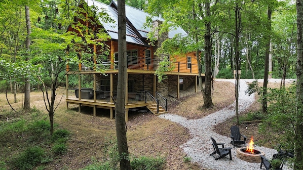 A cabin with a stone foundation and wooden upper levels, surrounded by a forest.