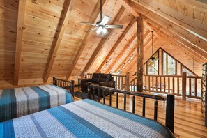 A cozy attic bedroom with two beds, a ceiling fan, and a view of the outdoors.