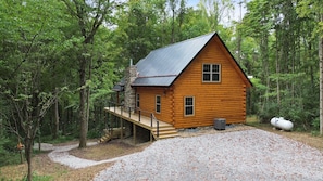 A log cabin with a metal roof, a deck, and a gravel driveway.
