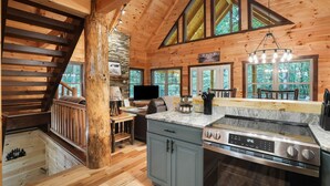 A wooden cabin interior with a kitchen, dining area, and a staircase.