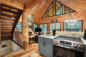 A wooden cabin interior with a kitchen, dining area, and a staircase. - The Lazy Bear | Hocking Hills, Covered Hot Tub (Logan)