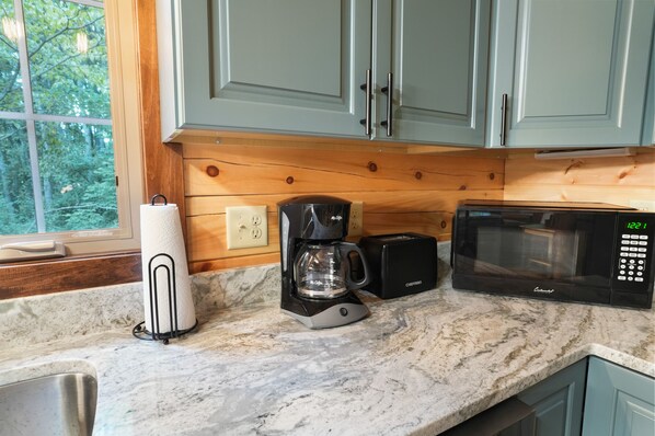 A kitchen with a coffee maker, a microwave, and a window with a view of trees.