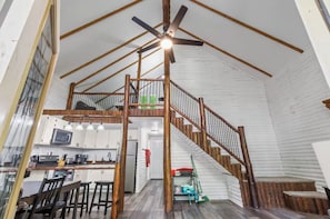 Amplia habitación estilo loft con escalera de madera, zona de cocina y comedor.