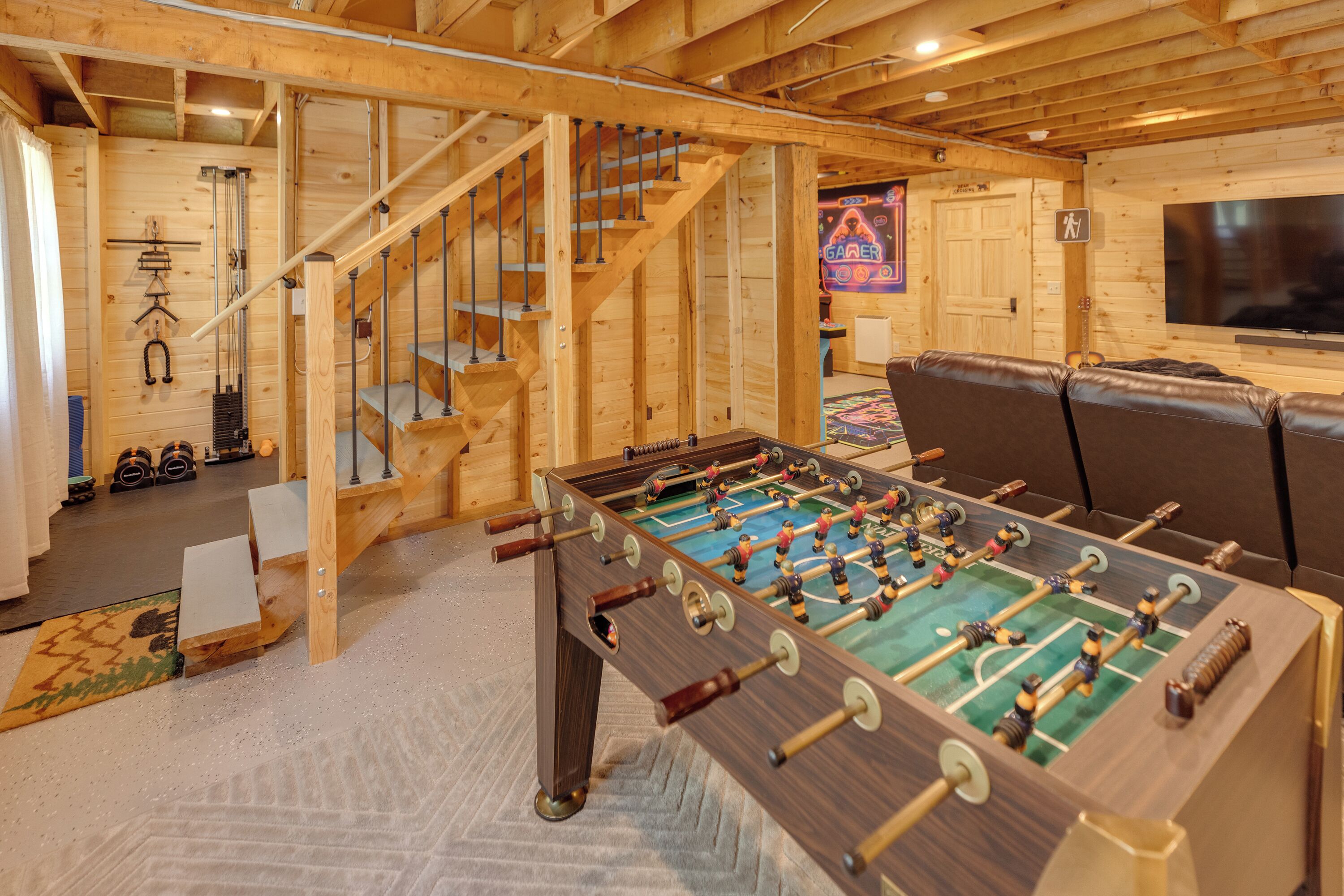 A wooden-floored room with a foosball table, a sofa, and a staircase.