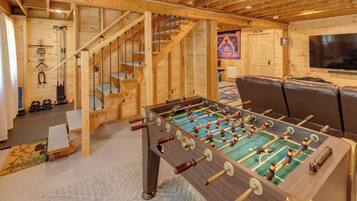 A wooden-floored room with a foosball table, a sofa, and a staircase.