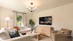 Un salón con sofá, sillón, mesa de centro y una pantalla de Netflix instalada en la pared.